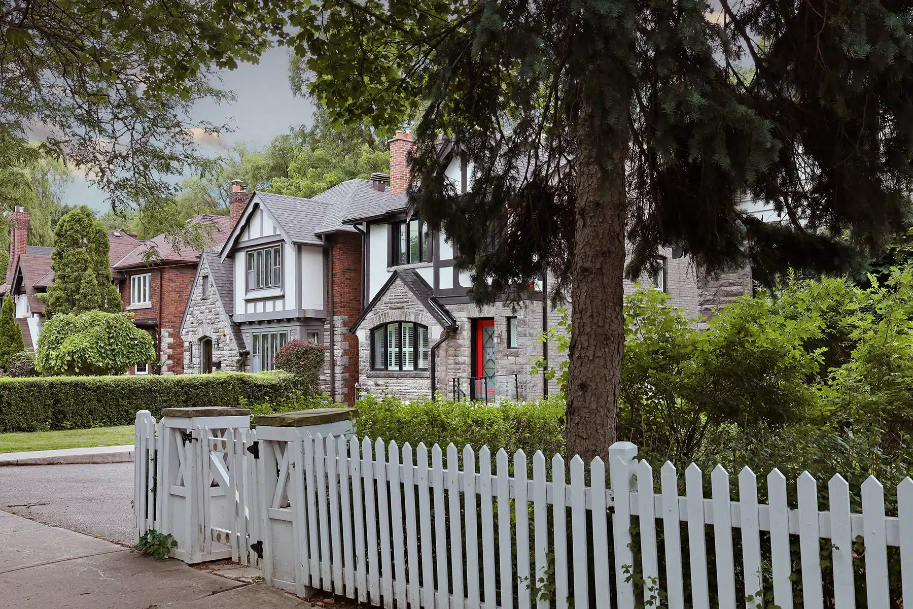 Classic white picket fence bordering a well-manicured lawn with homes and a blue sky.